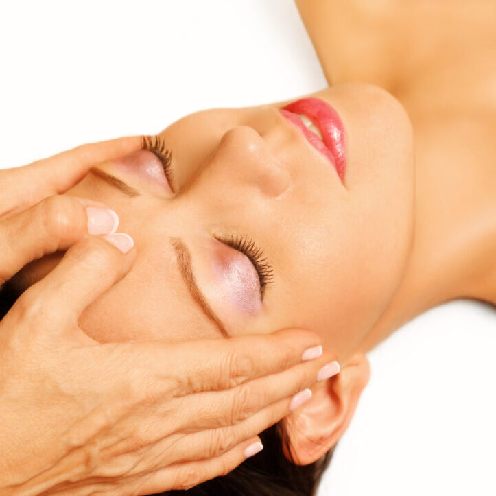 Young woman lying on her back, gets massage,reiki,acupressure on her head, focus on face and hands